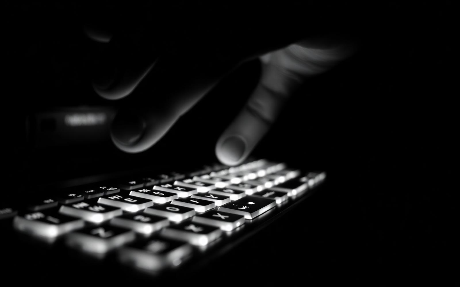 A hand poised over an illuminated keyboard in near darkness, motion blur on the fingers.